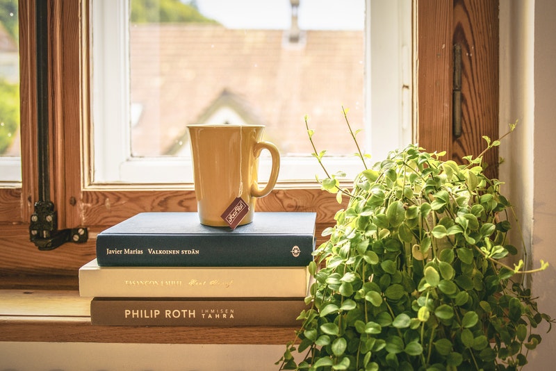 木製サッシの窓のそばにあるコーヒーと本
